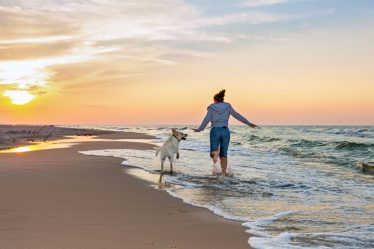 Photo d'une femme qui cours sur la plage avec son chien